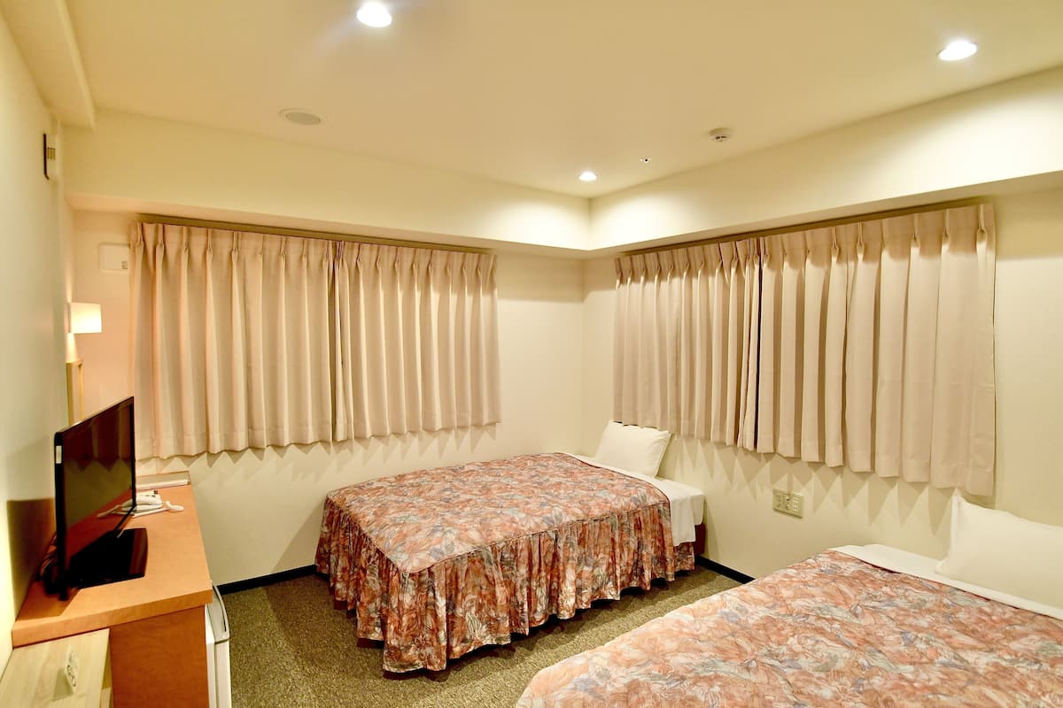 Een hotelkamer met twee bedden, een bureau met een televisie, en gordijnen voor de ramen.