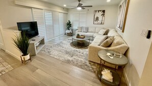 A modern living room with a sofa, coffee table, TV, and a ceiling fan. - Sea Oats 3BR-Direct Beach Access with Pool (Cocoa Beach)