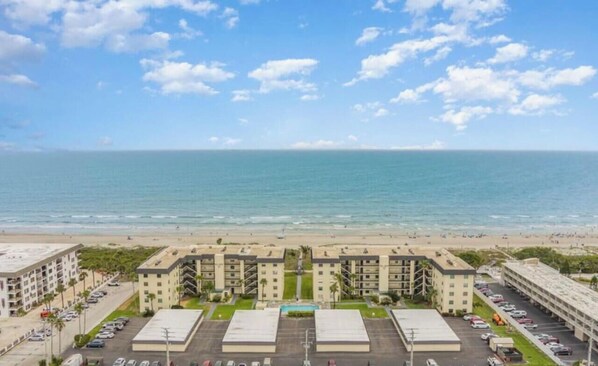 A beachfront hotel with multiple buildings, a parking lot, and a view of the ocean. - Sea Oats 3BR-Direct Beach Access with Pool (Cocoa Beach)