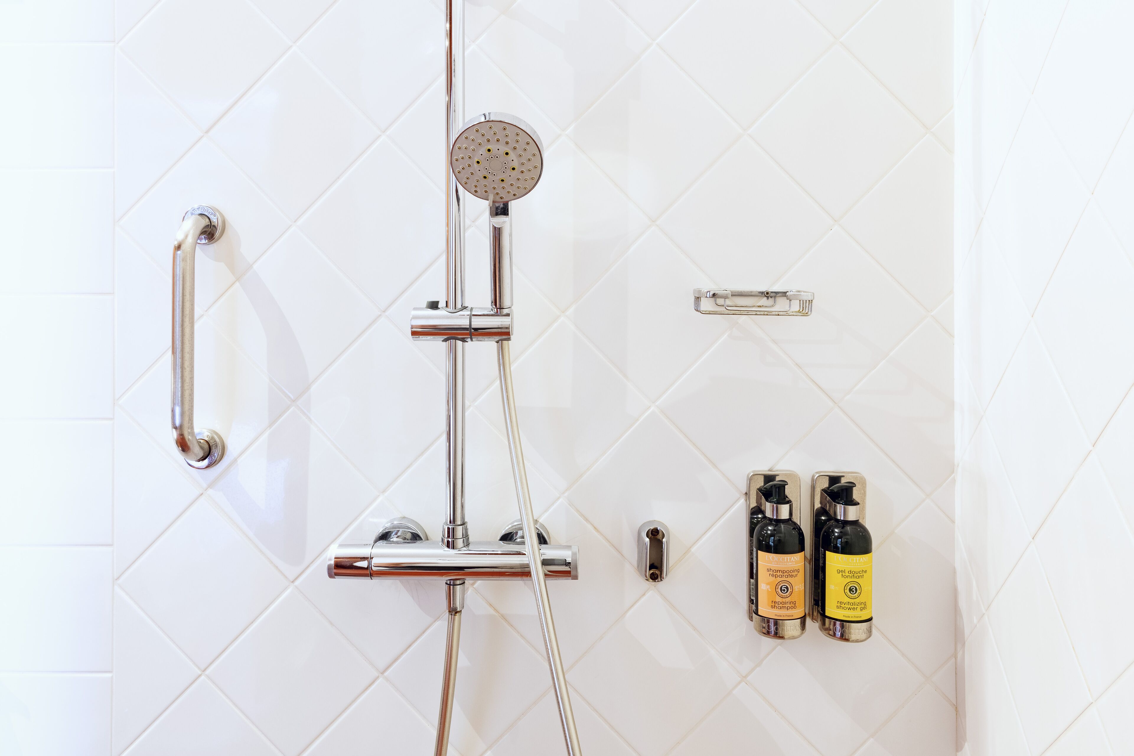 A shower with a handheld showerhead, a rain showerhead, and two bottles of shower products.