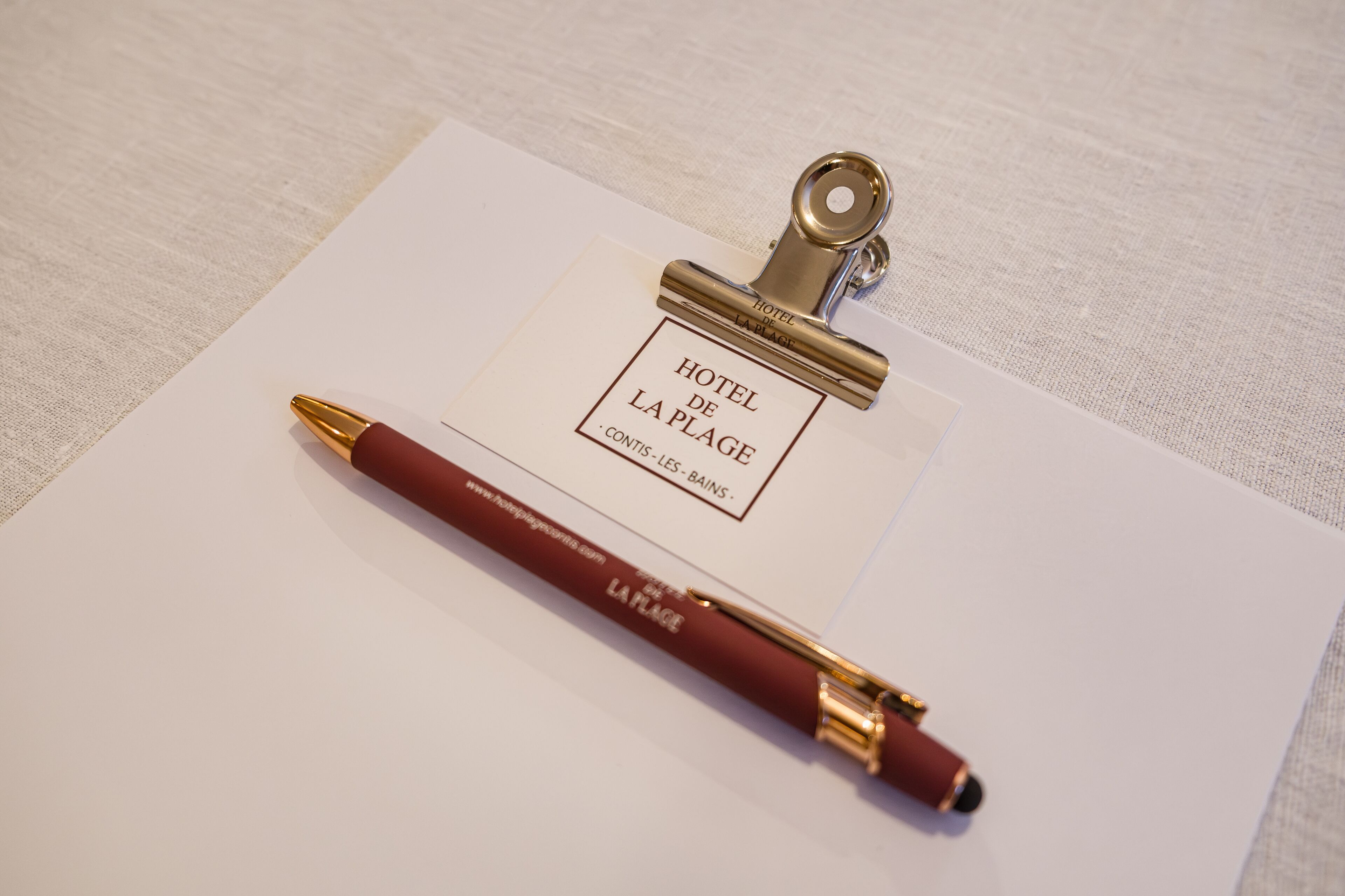 Un badge avec le nom de l’hôtel, un stylo et un presse-papiers sur une surface blanche.