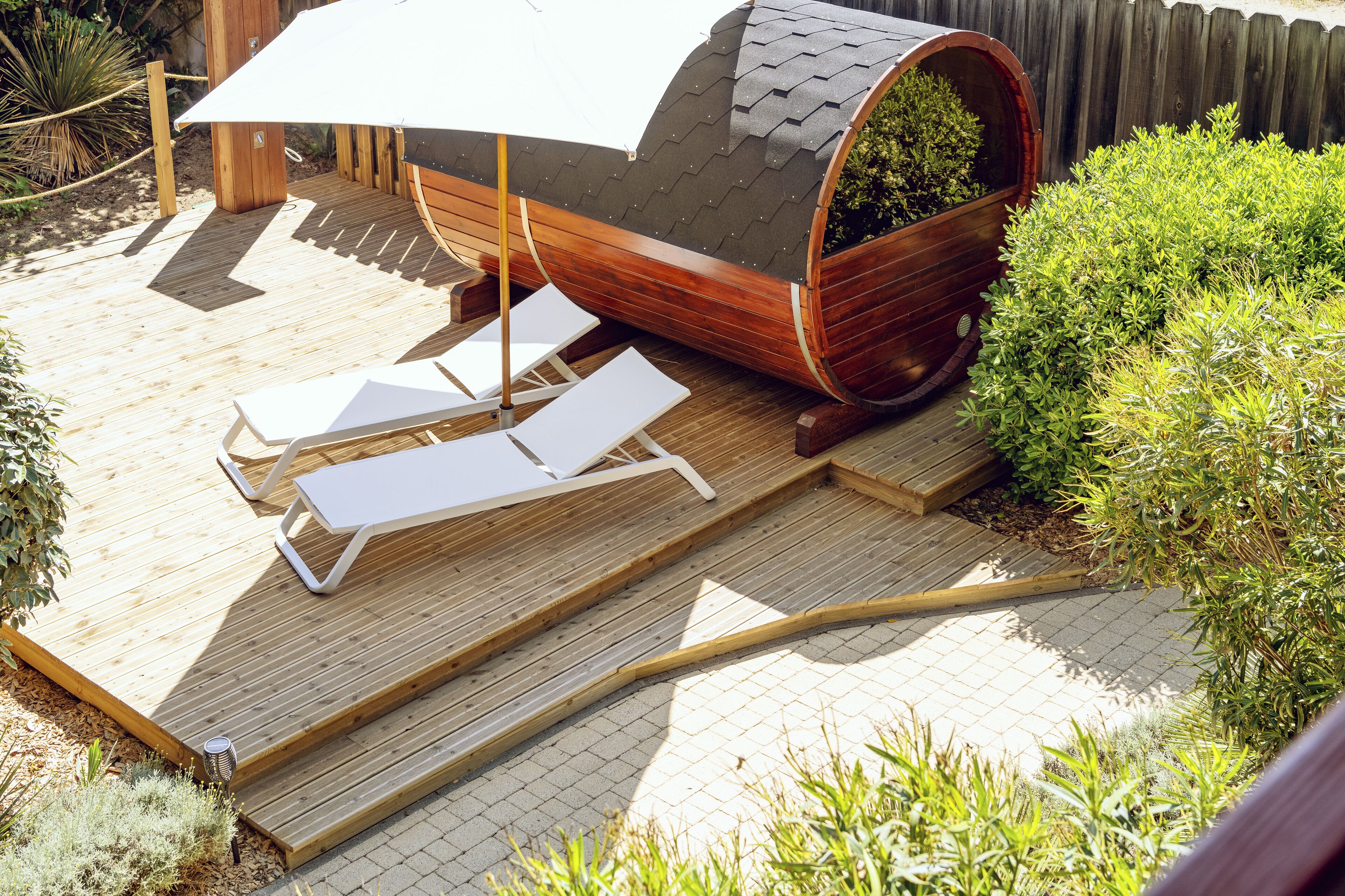 Une terrasse en bois avec deux chaises longues et un grand parasol.