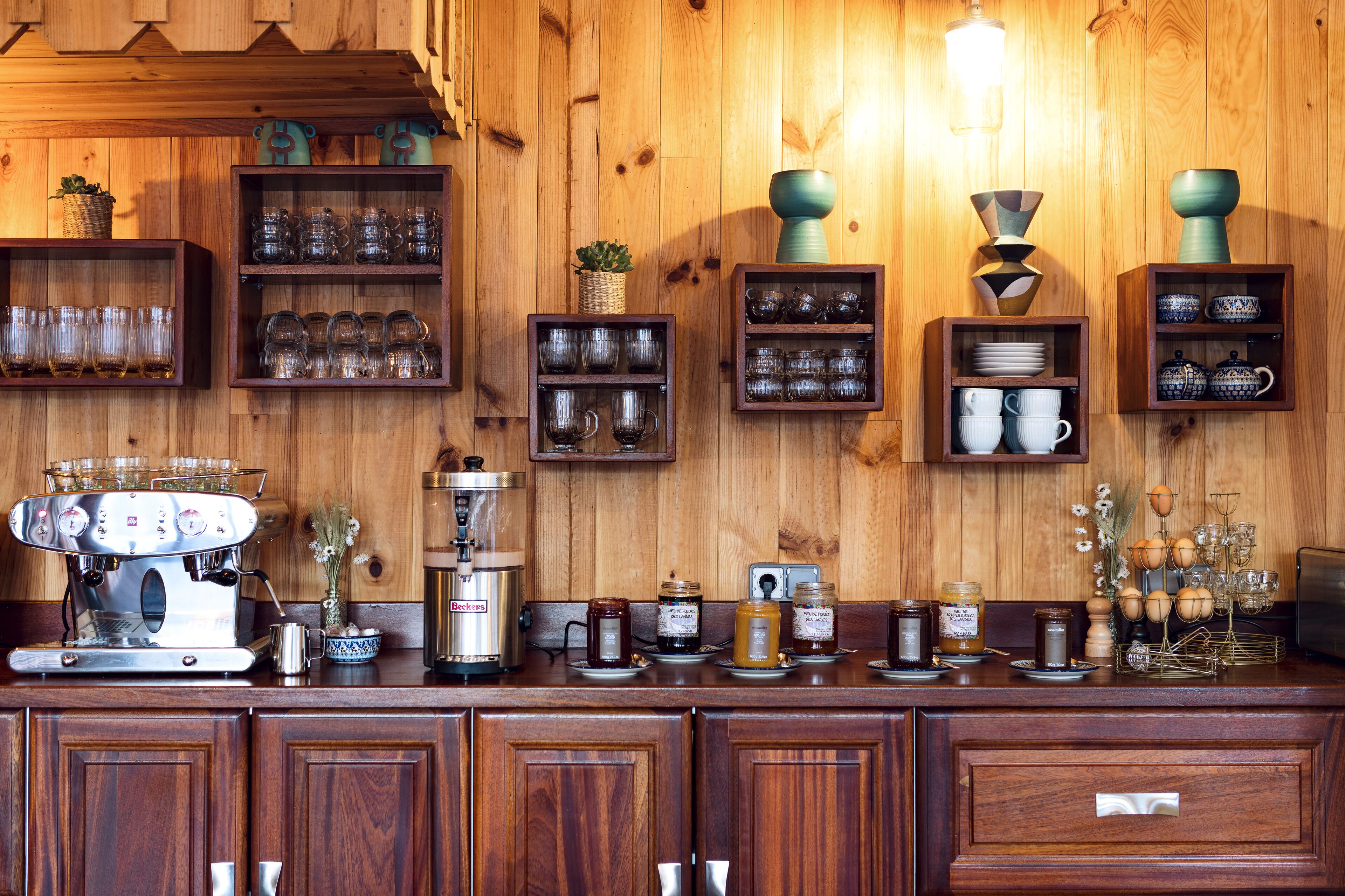 Un interior de madera con estantes que exhiben cristalería, una máquina de café y varios frascos.