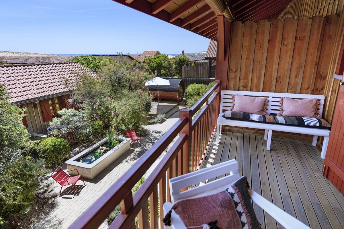 Une terrasse en bois avec un banc blanc et un petit espace jardin agrémenté d’un jardinier et de chaises rouges.
