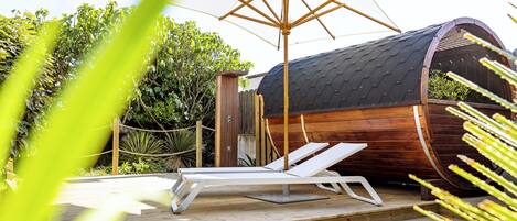 A wooden structure with a curved roof, a small deck with a white lounge chair, and a large umbrella.