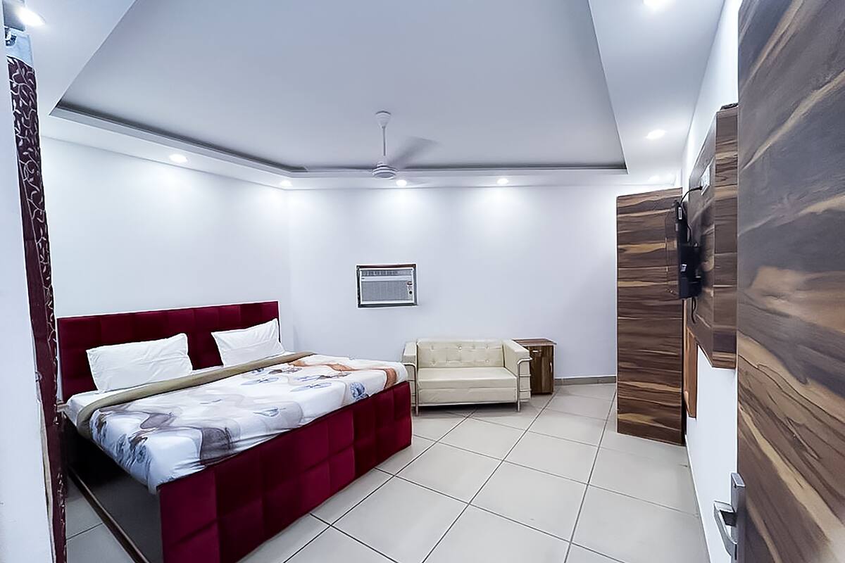 A bedroom with a bed, a sofa, a ceiling fan, and a wall-mounted TV.