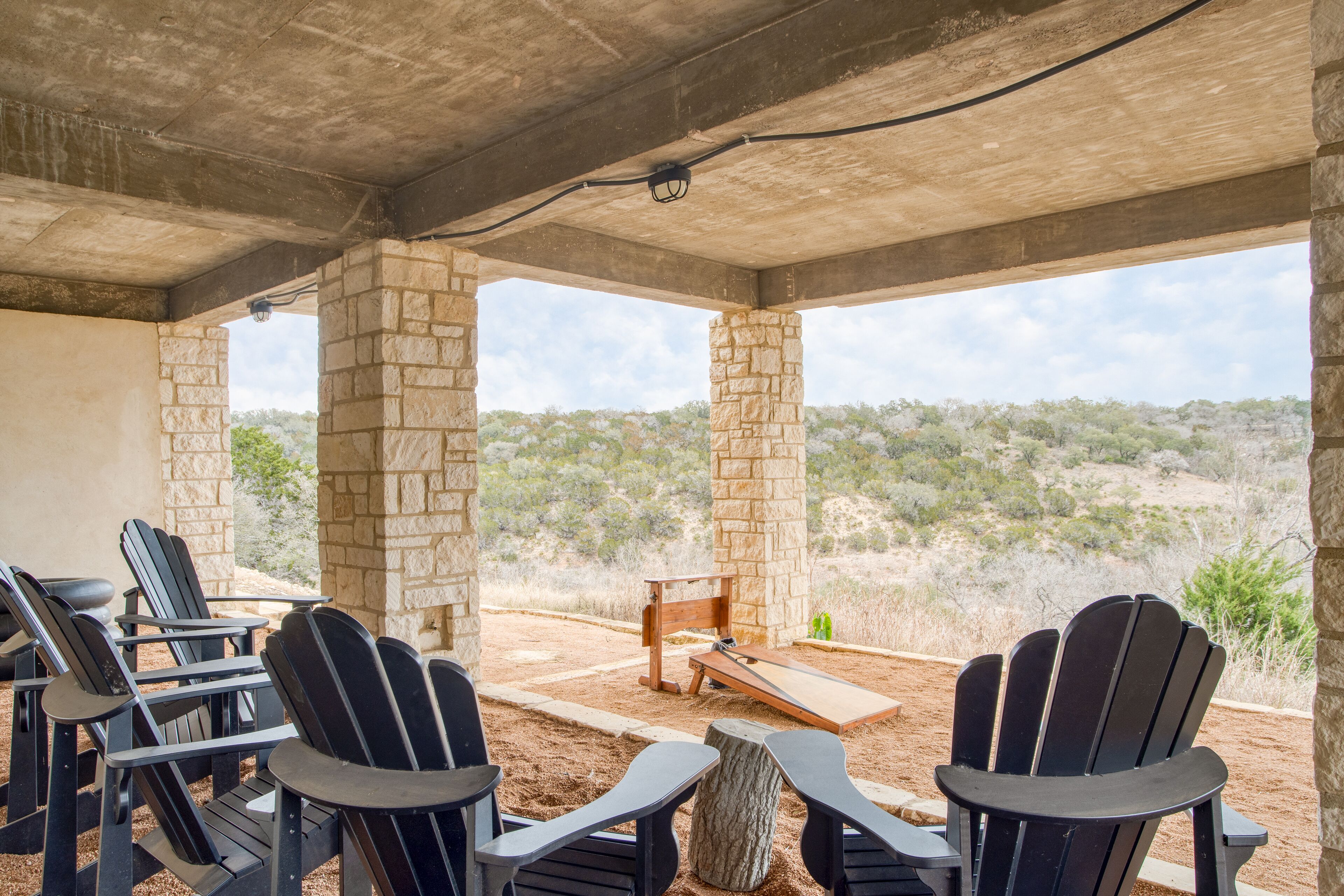 A covered outdoor seating area with stone pillars, black Adirondack chairs, and a wooden table.