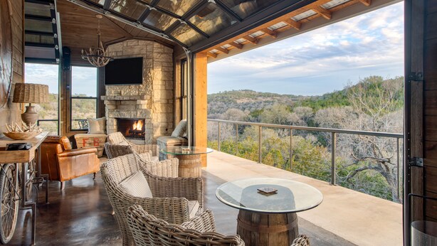 Un balcón amplio con mobiliario de mimbre, una chimenea de piedra y vistas del paisaje circundante.