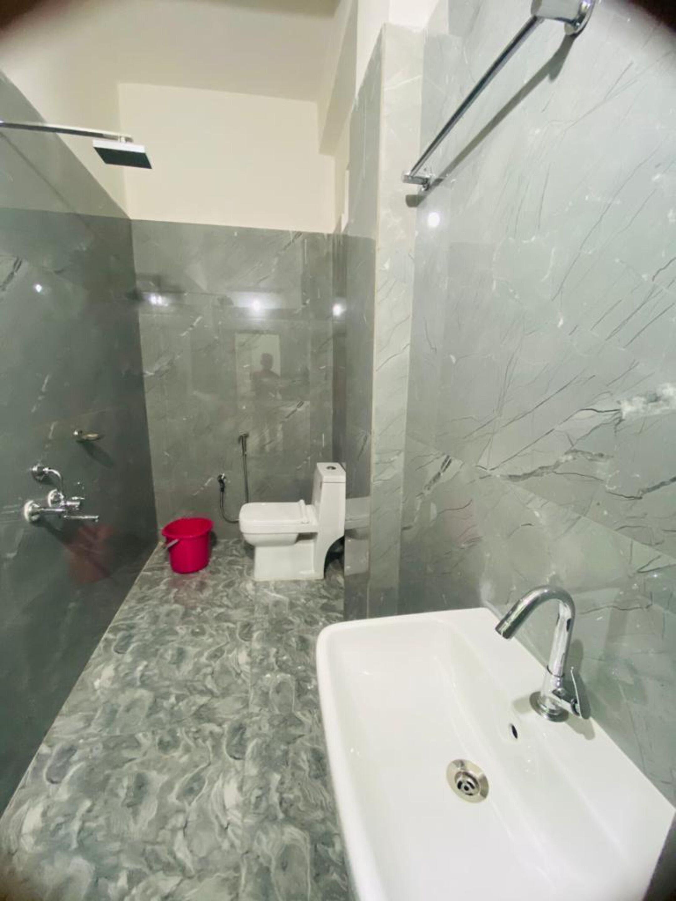 A bathroom with a marble floor, a white sink, a red bucket, and a toilet.