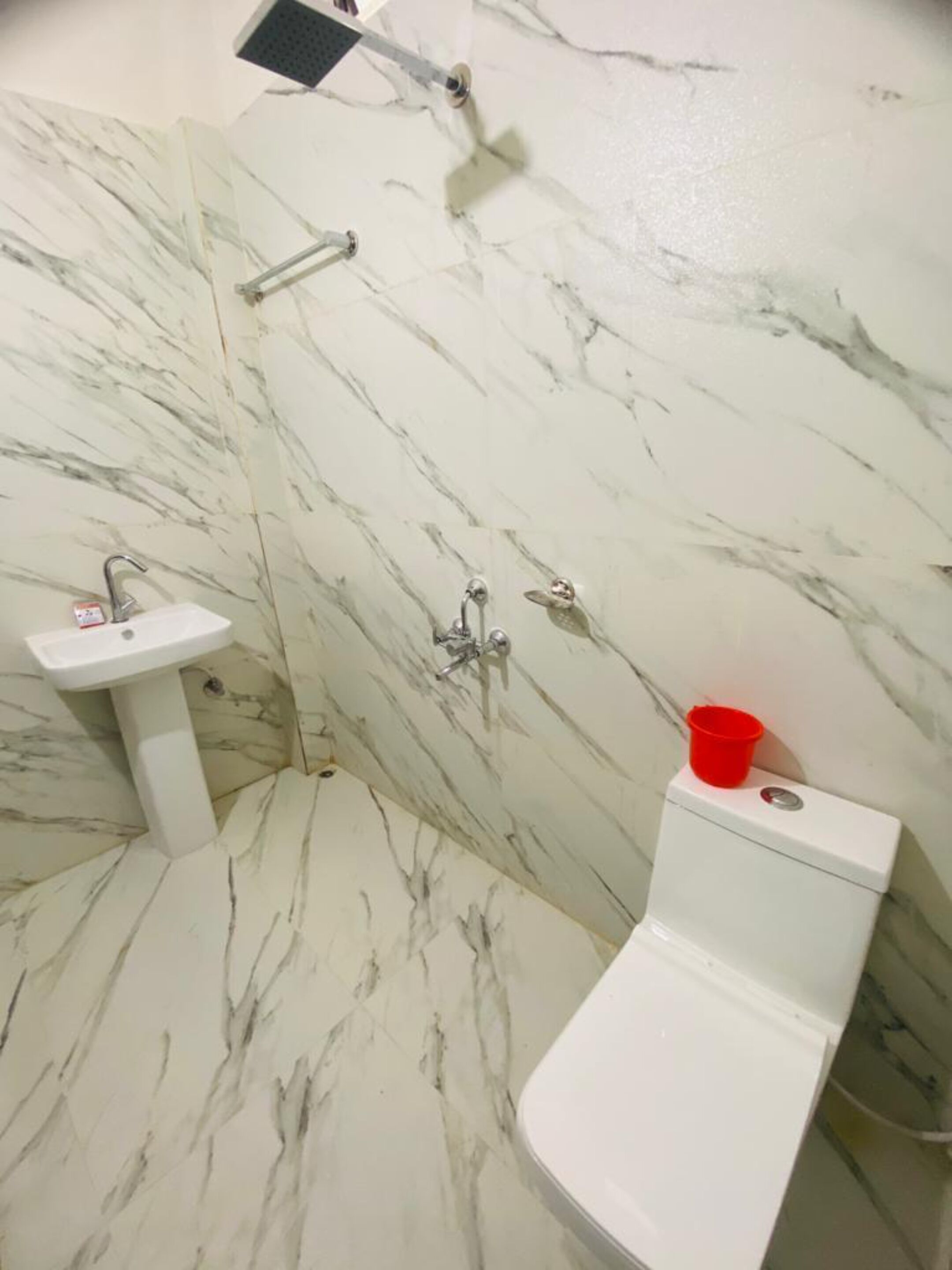 Une salle de bain avec un sol en marbre, un lavabo blanc, des toilettes et une pomme de douche.
