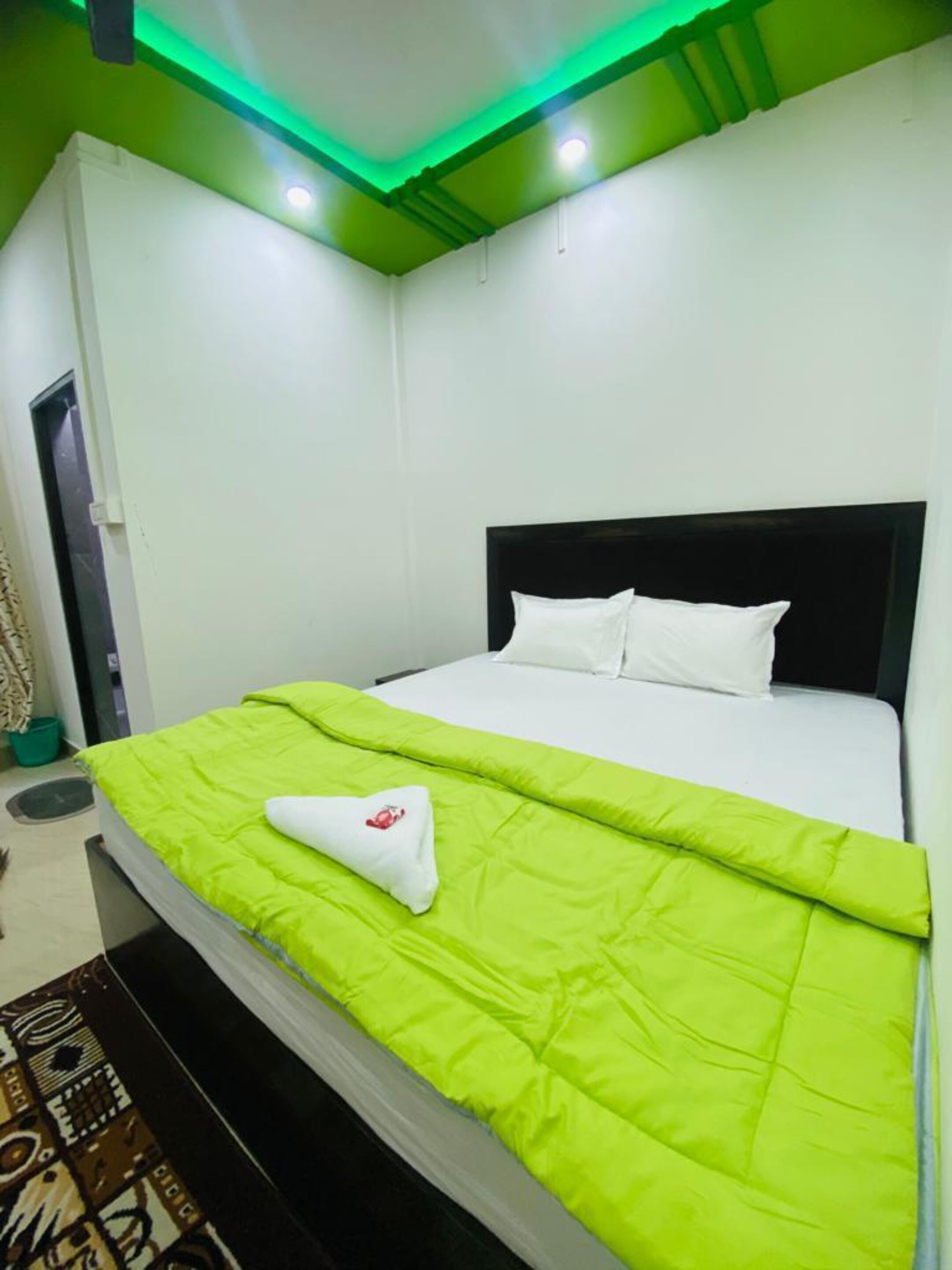 Una habitación de hotel con cama, ropa de cama verde, cabecera negra y lámpara de techo verde.