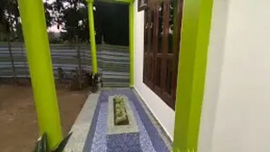 A covered outdoor area with a tiled floor, green pillars, and a door. - Kaziranga Inn (Bokakhat)