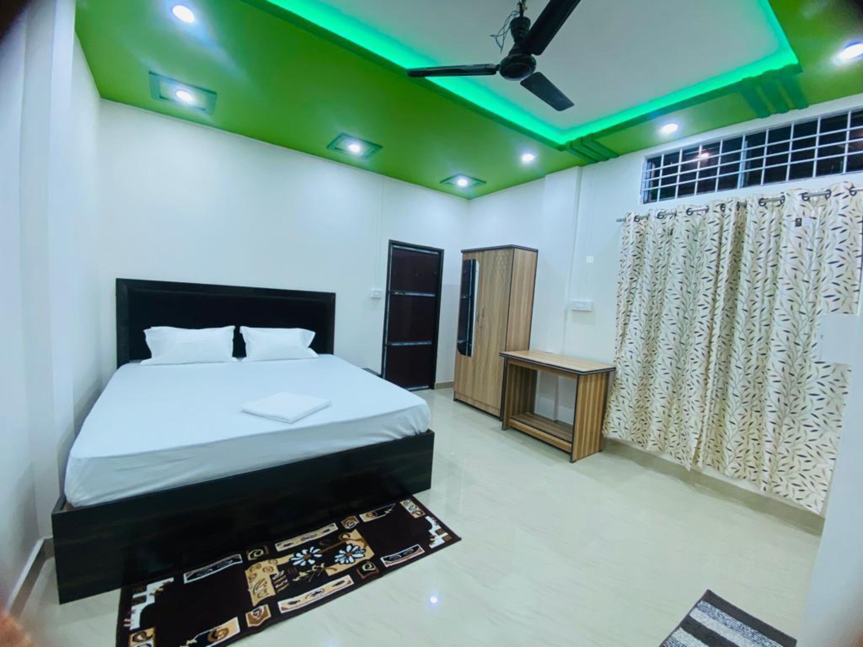 A modern bedroom with a bed, a wardrobe, a desk, and a ceiling fan.