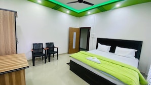 A hotel room with a bed, two chairs, a desk, and a ceiling fan. - Kaziranga Inn (Bokakhat)