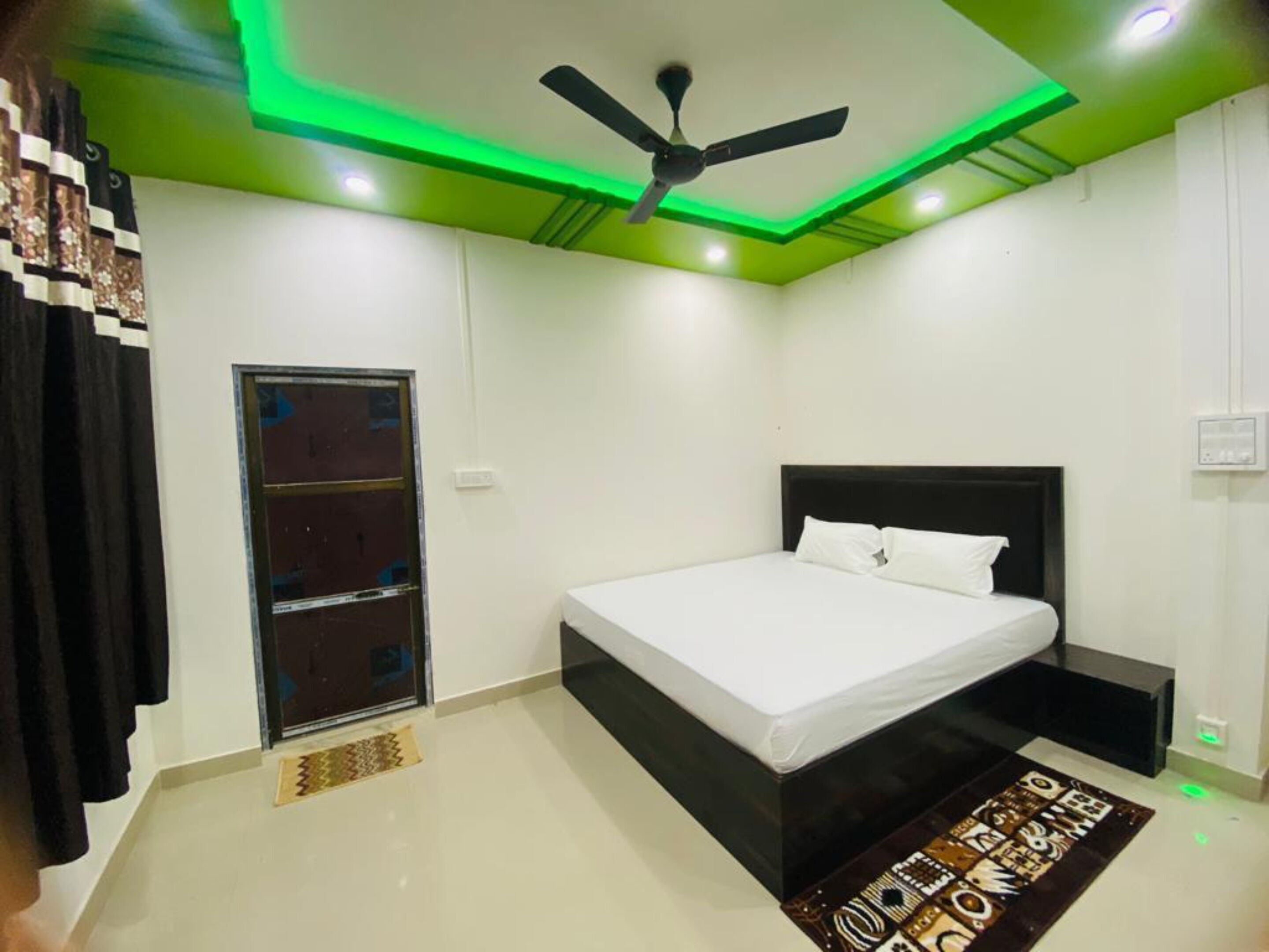 Une chambre à coucher avec un lit, un ventilateur de plafond, une fenêtre et une porte.