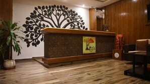A reception desk with a decorative tree mural, a logo, and a potted plant. - Shri Nilayam Kutir (Varanasi)