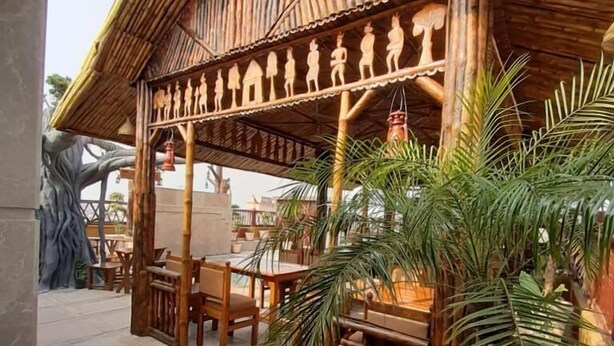 A covered outdoor seating area with wooden furniture and a decorative bamboo roof. - Shri Nilayam Kutir (Varanasi)