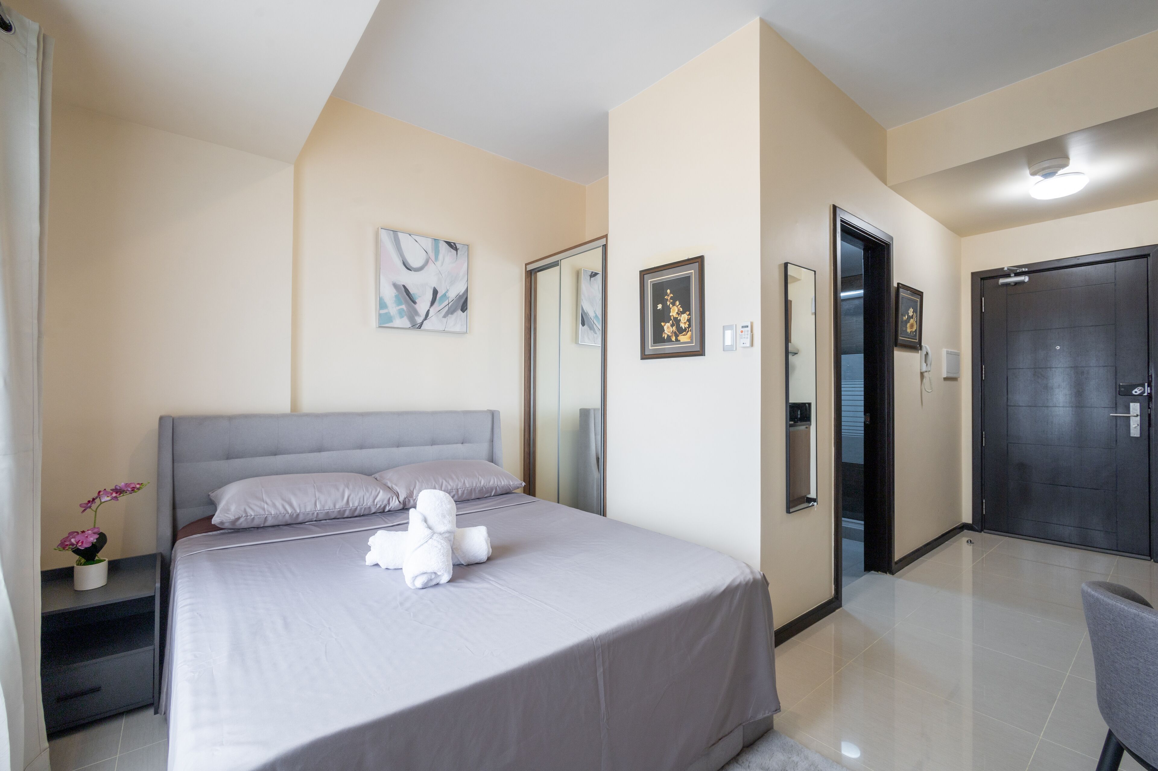 A neatly arranged bedroom with a bed, bedside tables, a mirror, and a door.