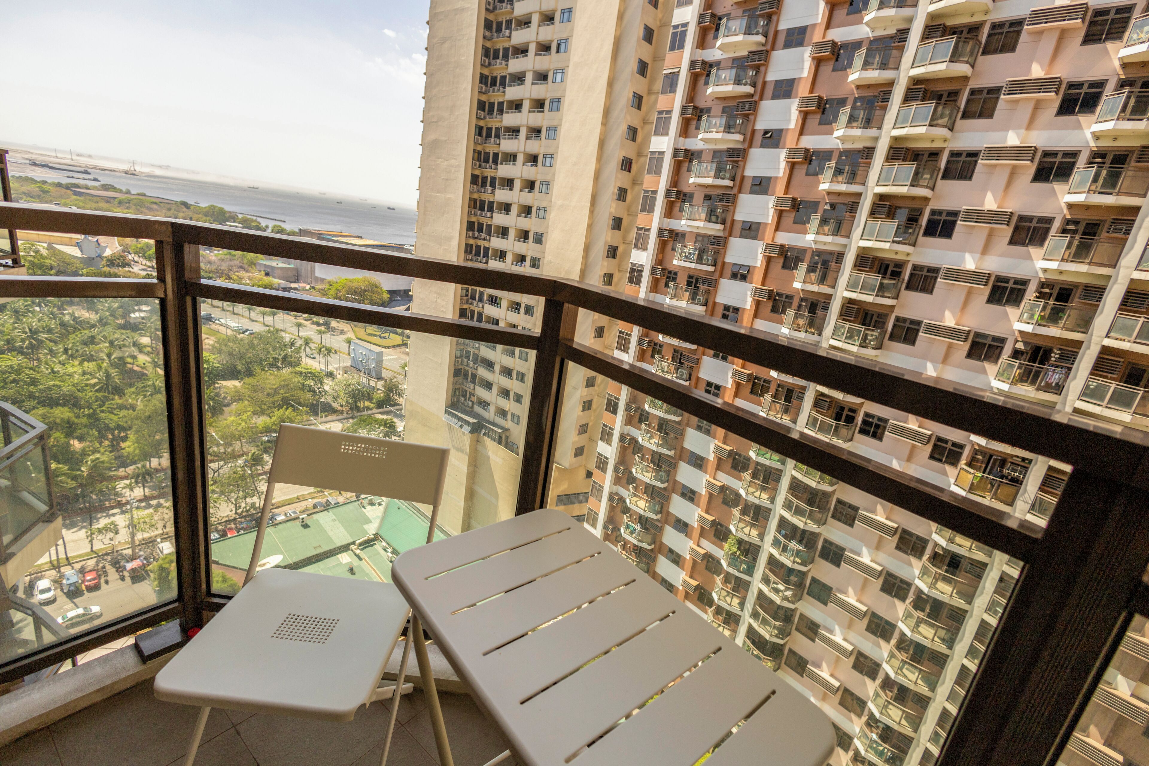 A balcony with a table and chairs, overlooking a high-rise building and a beach.