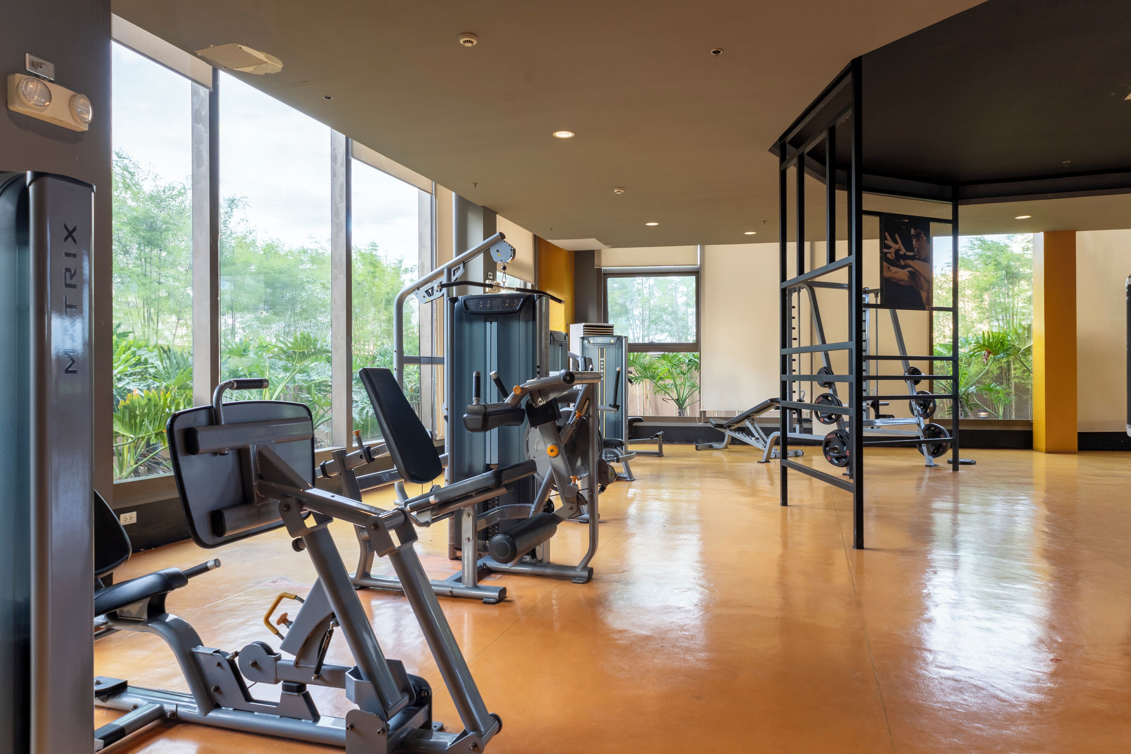 A gym with various exercise machines, large windows, and a polished wooden floor.