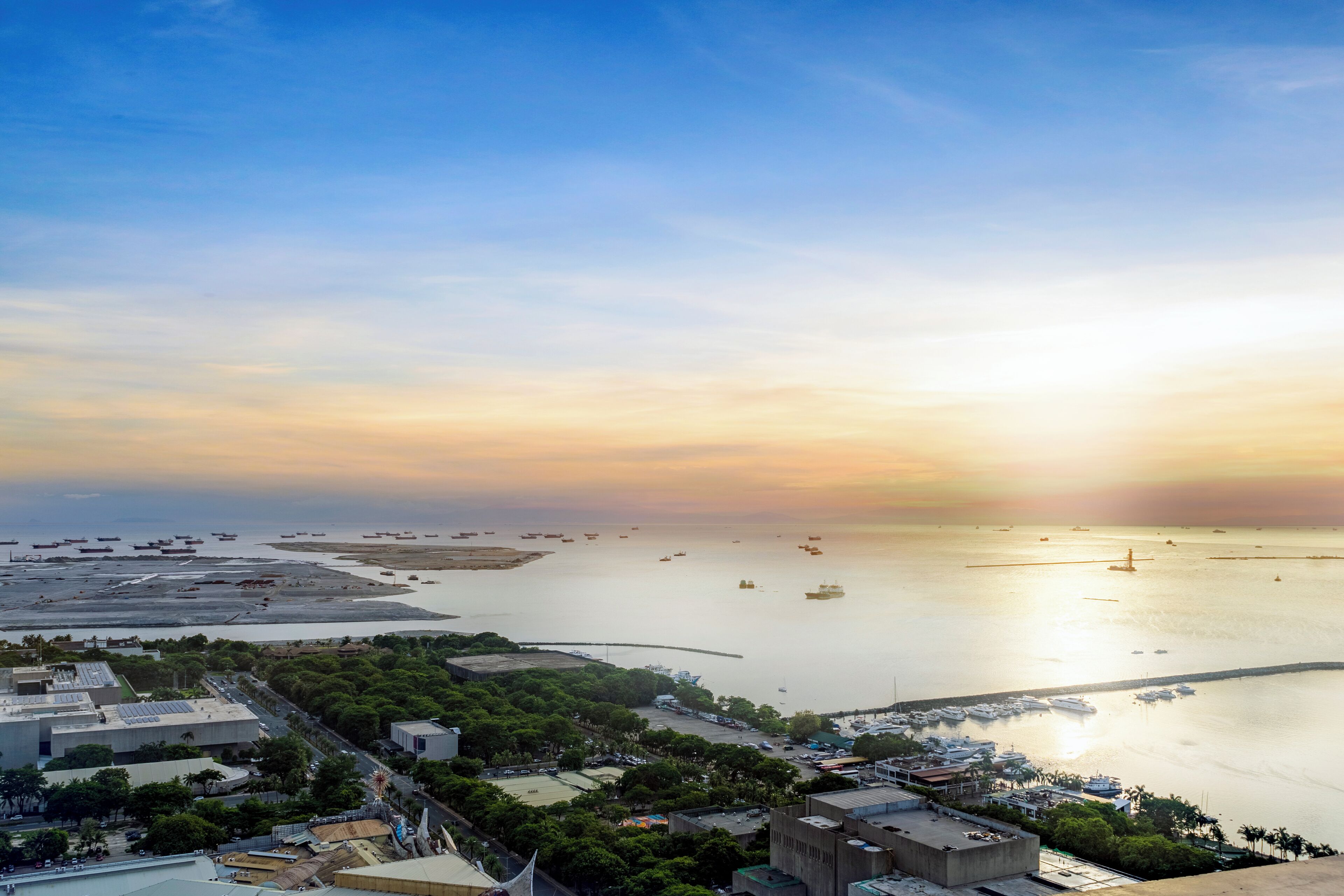 A coastal cityscape with a marina, buildings, and a sunset.