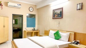 A hotel room with a bed, bedside table, and a desk with a chair. There is a clock on the wall and an air conditioning unit above the desk. - Quang Chung Hotel Long Bien- Bay Luxury (Hanoi)