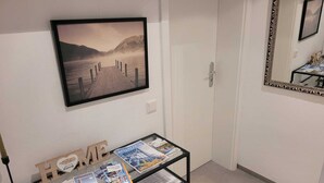 A hallway with a framed picture of a lake and mountains, a glass table displaying brochures, and a mirror on the wall. - Ferienwohnung Hereinspaziert (Wilhelmshaven)