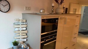 A modern kitchen with a wooden table, a clock, and a signpost with directional signs. - Ferienwohnung Hereinspaziert (Wilhelmshaven)