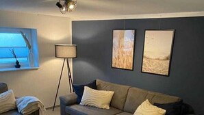 A living room with a sofa, a coffee table, and two wall-mounted pictures. - Ferienwohnung Hereinspaziert (Wilhelmshaven)