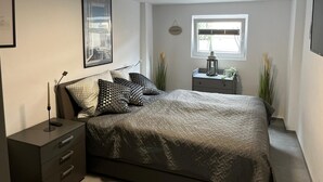 A bedroom with a bed, bedside tables, a window, and a ceiling light. - Ferienwohnung Hereinspaziert (Wilhelmshaven)