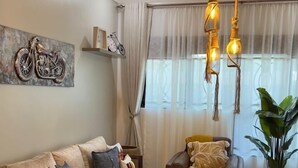 Ein Wohnzimmer mit einer Couch, Sesseln, einem Couchtisch, einem Motorrad-Kunstwerk, einer Chandelieber und einem großen Fenster mit Vorhängen.
