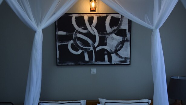Ein Bett mit Baldachin, ein Nachttisch mit Pflanze und ein an der Wand befestigtes Kunstwerk.