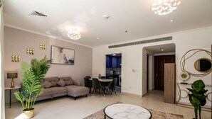 A modern living room with a sectional sofa, dining table, and chairs, a small coffee table, and decorative plants. - Yogi - Marina Marvel Luxurious 1BR Apt at Al Shera Tower (Dubai)