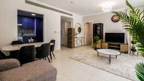 A modern living room with a dining area, a TV, and a kitchen visible through an open door. - Yogi - Marina Marvel Luxurious 1BR Apt at Al Shera Tower (Dubai)