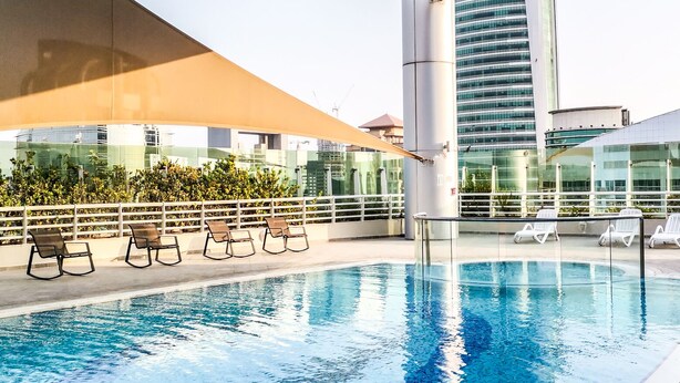 A rooftop pool with lounge chairs and a glass balustrade. - Yogi - Marina Marvel Luxurious 1BR Apt at Al Shera Tower (Dubai)