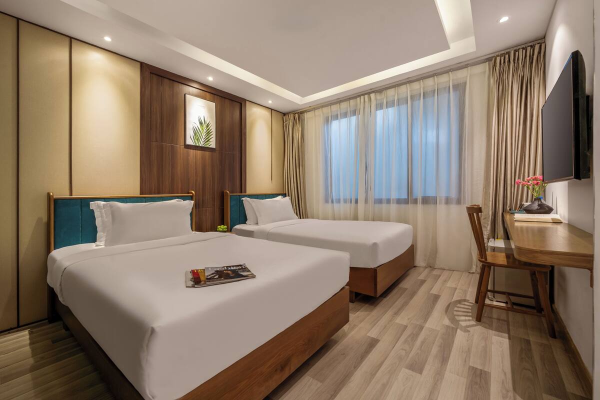 Habitación de hotel con dos camas, un escritorio de madera, una silla, un televisor y una ventana con cortinas.