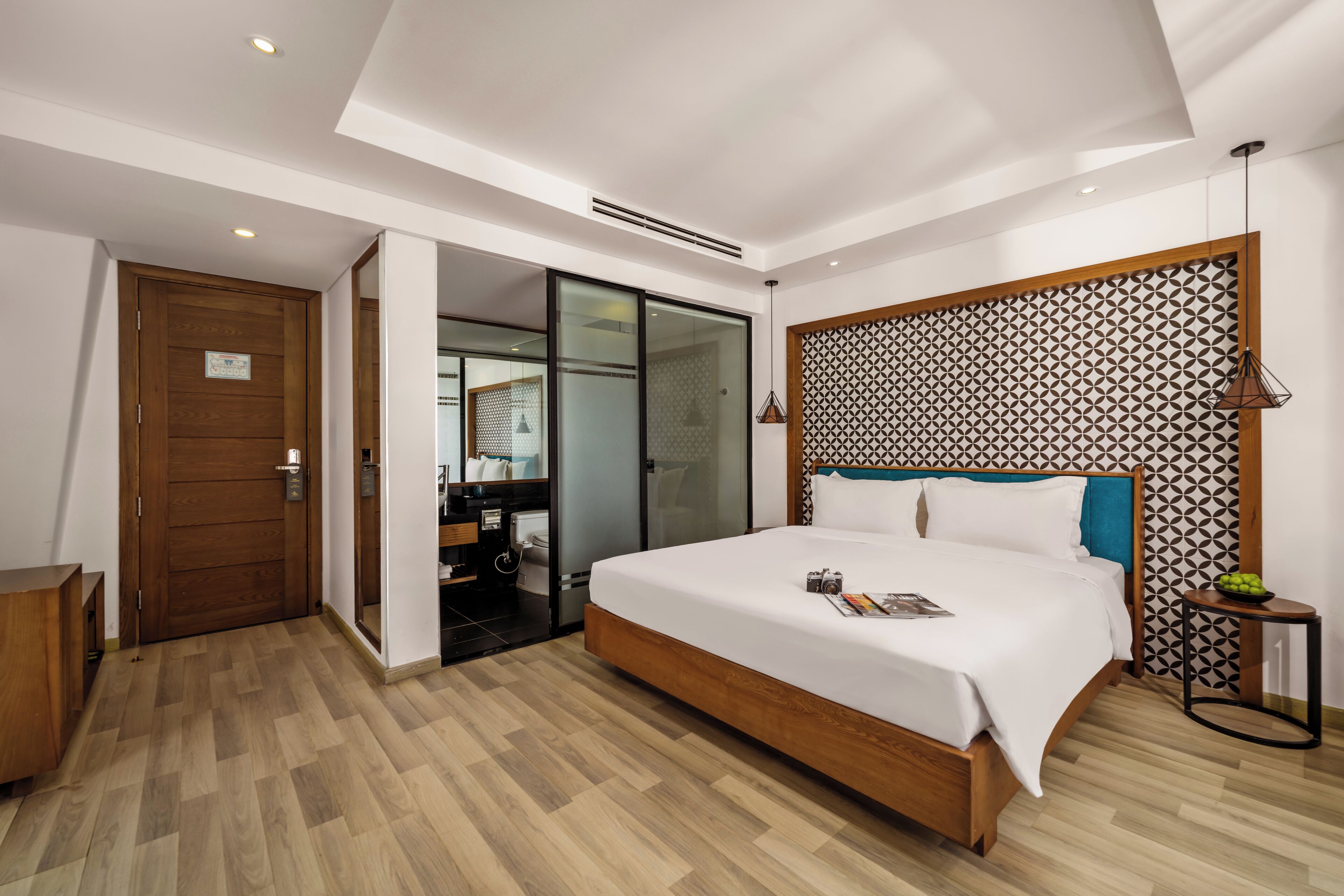 Quarto de hotel moderno com cama de madeira, porta de vidro para um banheiro e cabeceira estampada.