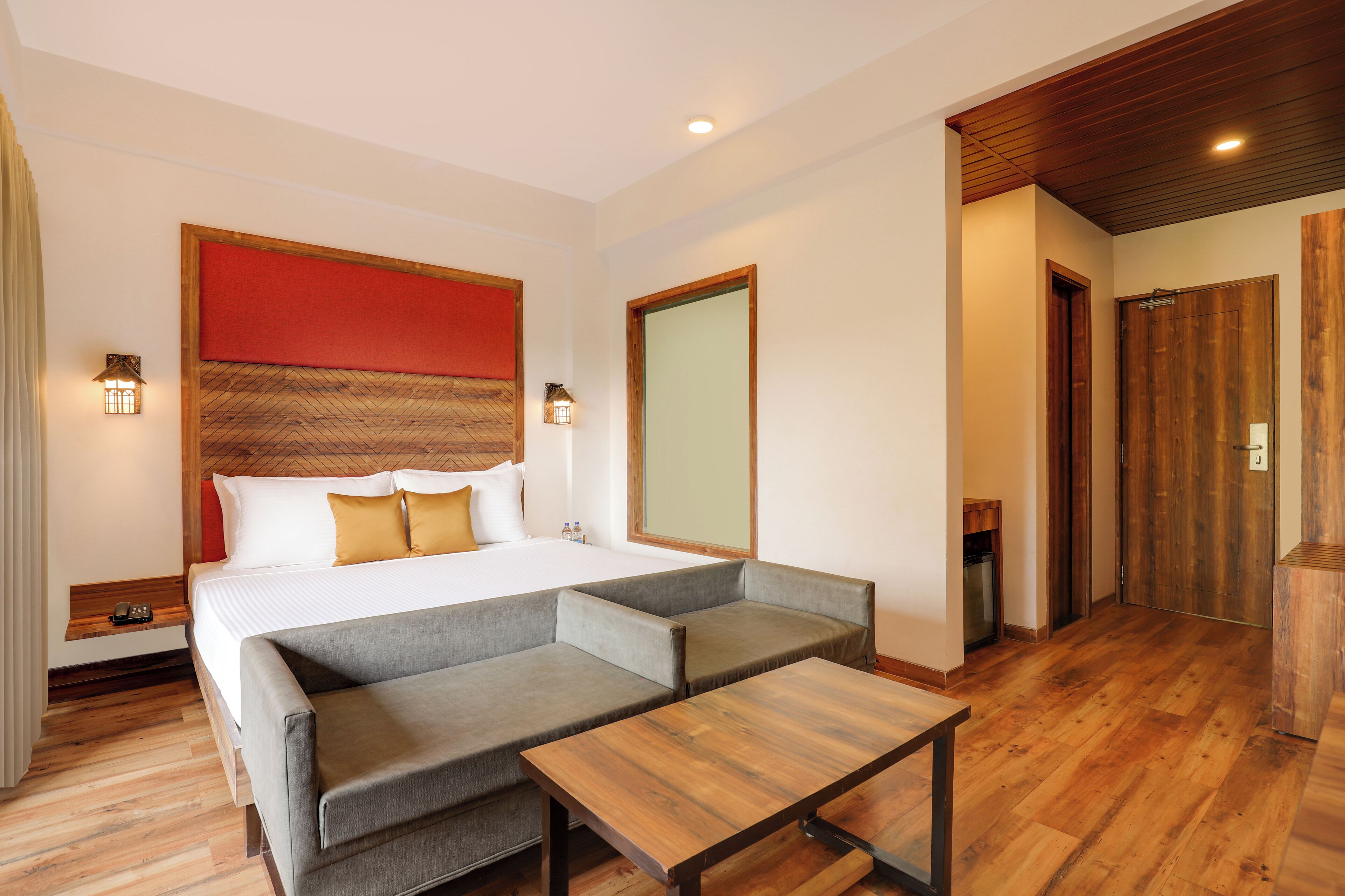 Una habitación de hotel con cama, sofá gris, mesa de madera y techo de madera.
