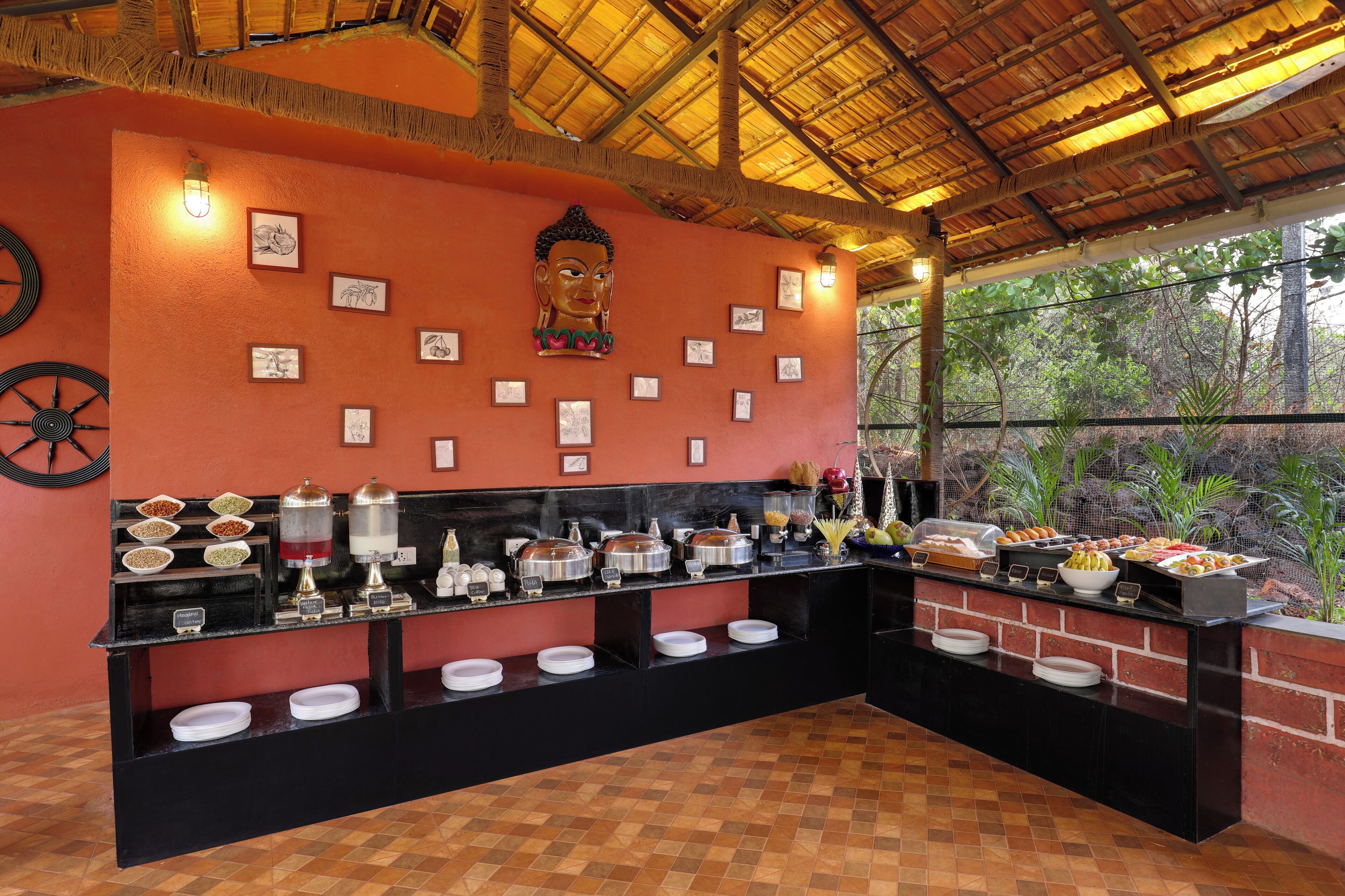Un buffet garni de divers plats et présentés dans différents récipients, une statue de Bouddha et une structure surmontée d’un toit de chaume.
