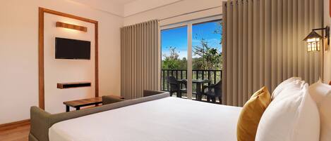 A hotel room with a large bed, a TV mounted on the wall, a balcony with chairs, and a view of the outdoors.