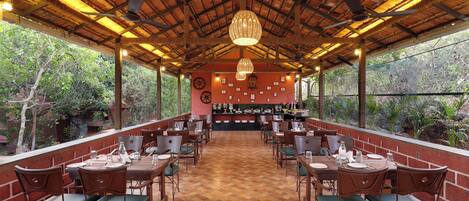 Un restaurante con techo de paja, mesas y sillas de madera, y vistas al exterior con vegetación.
