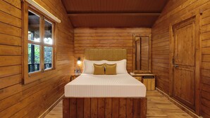 Un dormitorio de cabaña de madera con una cama, una mesita de noche, una ventana y una puerta.