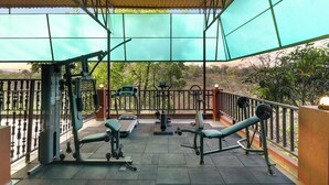 Un gimnasio al aire libre con diversos equipos de ejercicio, una zona cubierta con techo metálico y vistas al paisaje circundante.