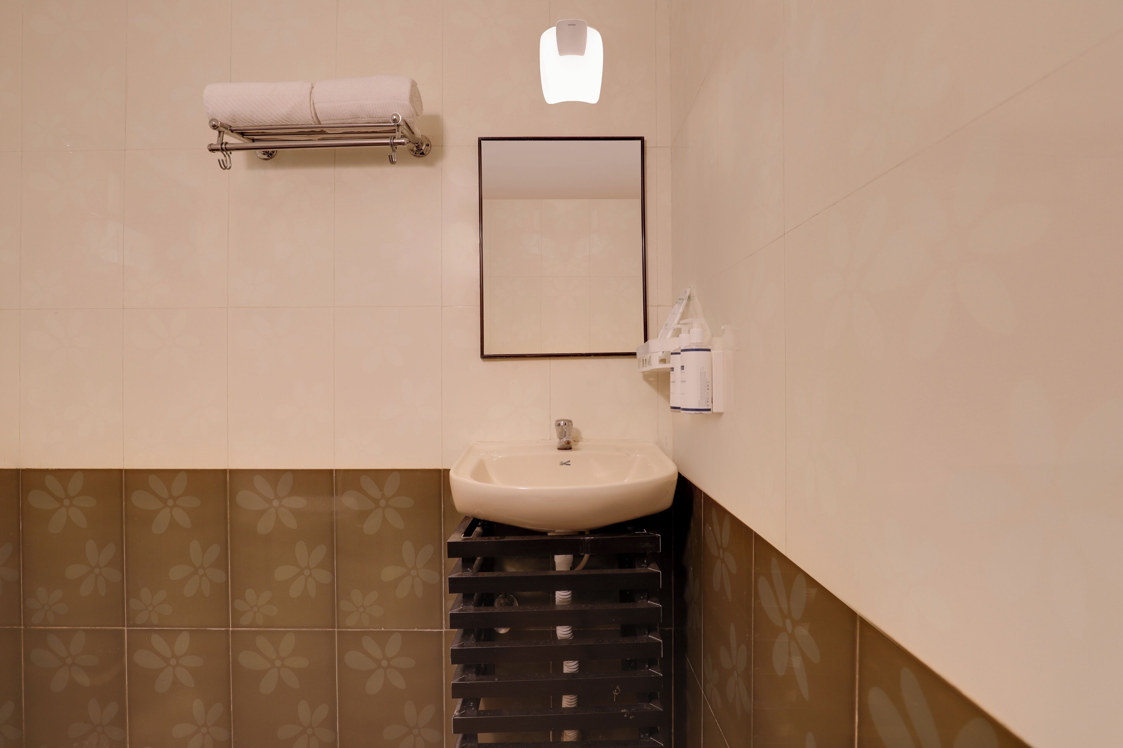 A bathroom with a sink, mirror, towel rack, and toilet paper dispenser.