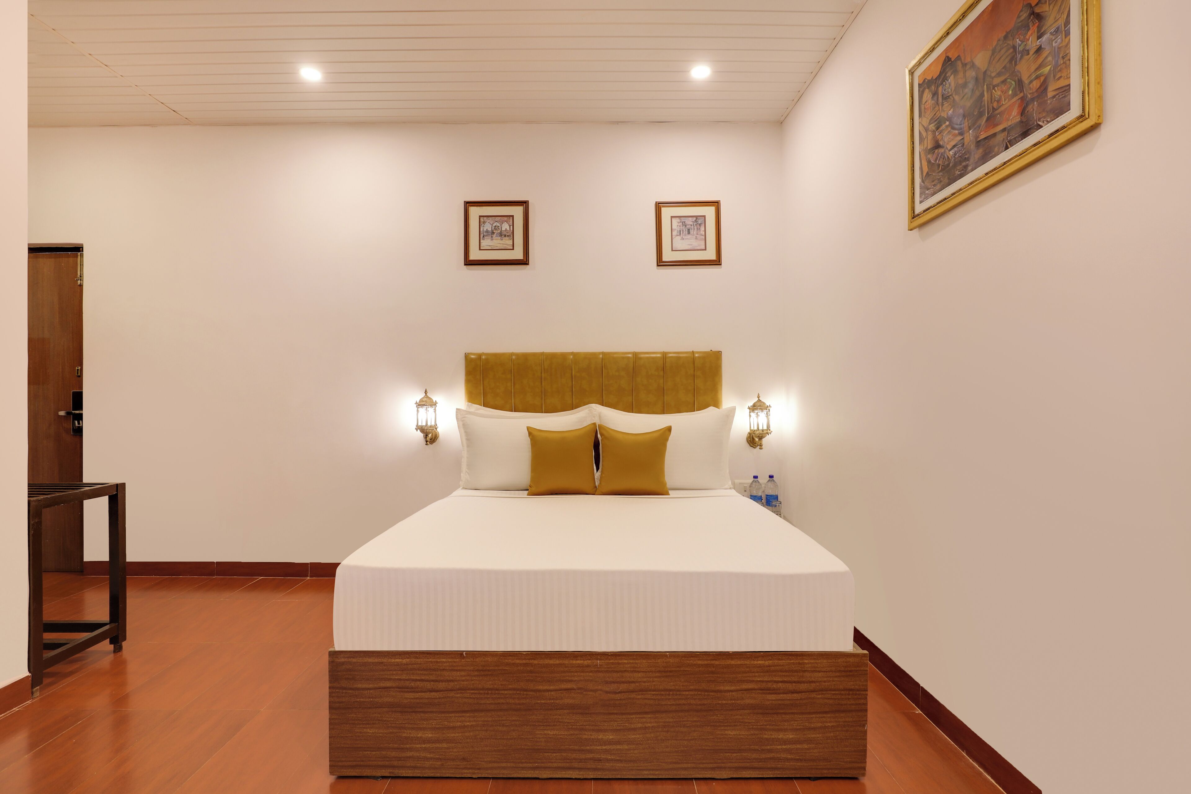 Un dormitorio ordenado con una cama grande, cabecera de madera, dos lámparas de pared y cuadros enmarcados en la pared.