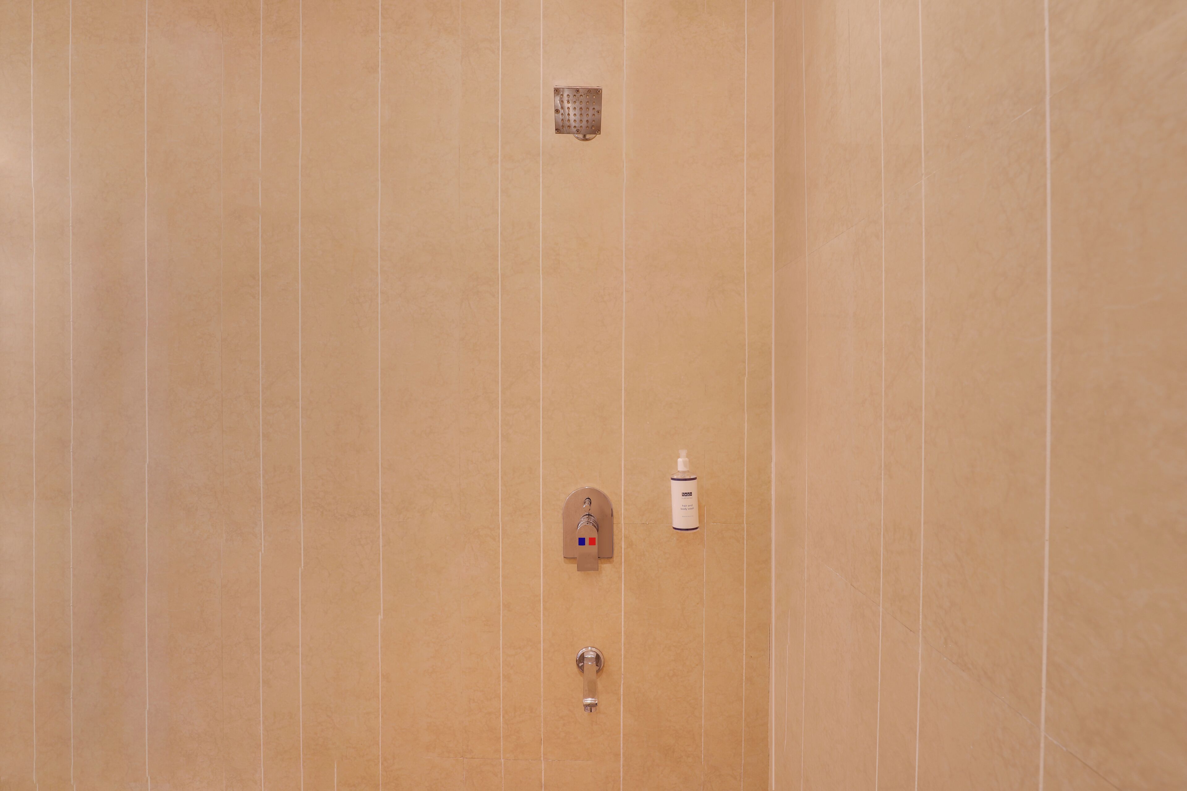Un baño con pared de azulejos color beige, ducha, dispensador de jabón y perchero para toallas.