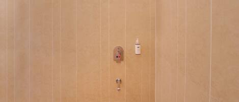 A bathroom with a beige tiled wall, a showerhead, a soap dispenser, and a towel rack.