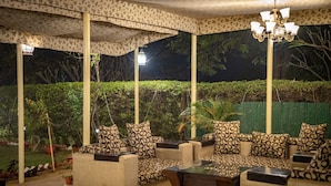 An outdoor seating area with patterned sofas and a glass coffee table, surrounded by greenery and a decorative canopy. - Sariska Tiger Heaven Resort (Thanagazi)