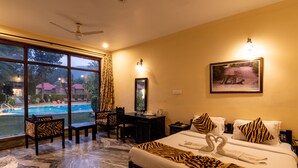 A hotel room with a large window, a desk, a chair, a bed with zebra-patterned bedding, and a framed picture on the wall. - Sariska Tiger Heaven Resort (Thanagazi)