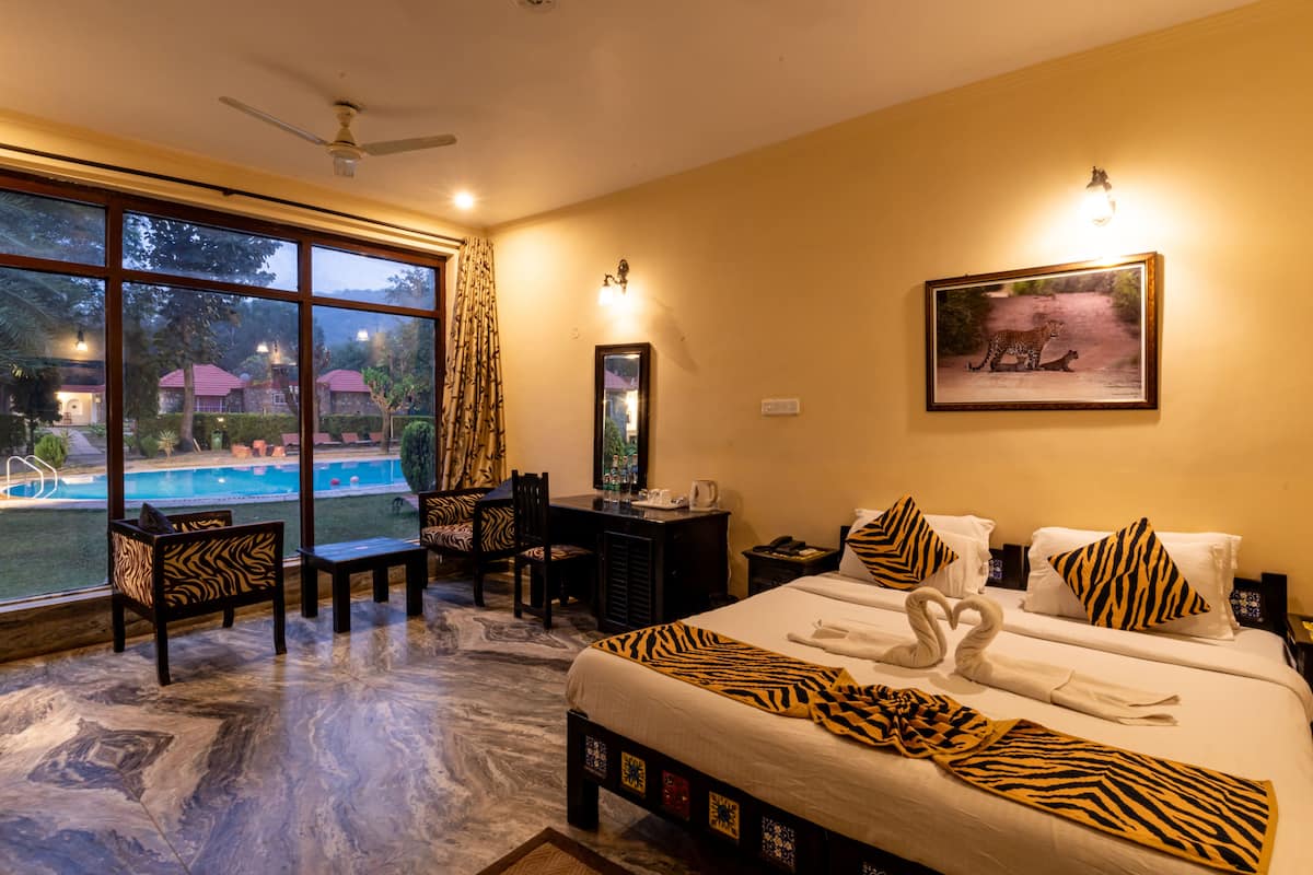 A hotel room with a large window, a desk, a chair, a bed with zebra-patterned bedding, and a framed picture on the wall.